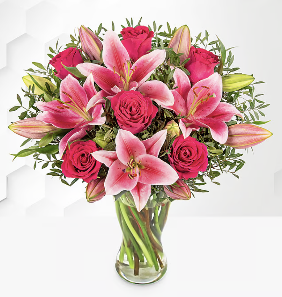 A vibrant bouquet featuring pink lilies and red roses, arranged with green foliage in a clear glass vase.